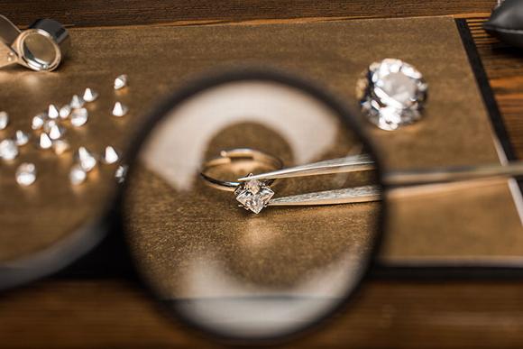 Ring on table at jewellers with tweezers picking up diamond 